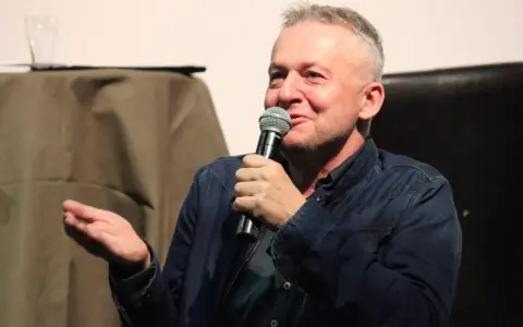 Bogusław Linda opowiada o swoich rolach w serialach i programach, trzymając mikrofon.