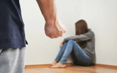 Zaciśnięta pięść mężczyzny grozi skulonej kobiecie. Scena symbolizuje agresję żony wobec męża, przemoc domową.