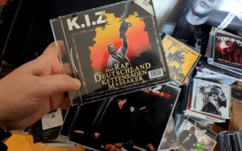 Hand hält CD-Cover von K.I.Z. "Das Rap Deutschland Kettensägen Massaker" mit Kettensäge.
