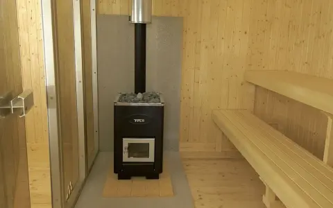 En nybyggd bastu utomhus med vedkamin, stenar och träbänkar. Perfekt för avkoppling.