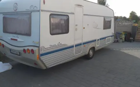 Biała przyczepa kempingowa TEC Travel King z niebieskimi pasami, gotowa na wakacyjne podróże.
