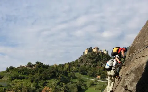 Zwei Kletterer am hoachwool Klettersteig mit Burg im Hintergrund.