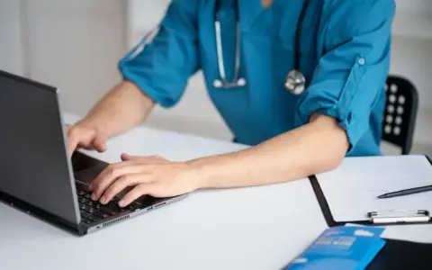 Lekarz medycyny pracy na laptopie, przygotowuje dokumentację. Zastanawiasz się, ile trwa wizyta u lekarza medycyny pracy?