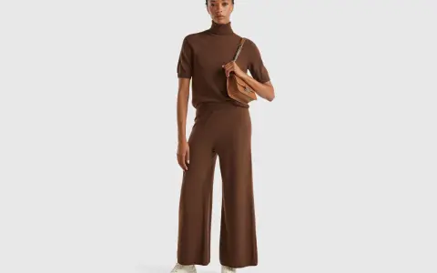 Mujer con conjunto marrón de cuello alto y pantalón ancho, bolso camel. Colores que combinan con el marrón, como el camel, resaltan la elegancia.