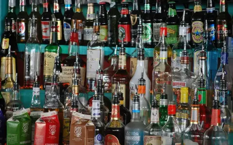 Różnorodne butelki alkoholi, w tym whisky, stoją na półce. Wskazówki, jak przechowywać whisky, mogą być przydatne przy tak bogatym asortymencie.