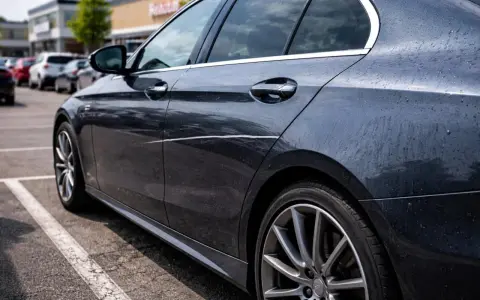Ciemny samochód na parkingu z widocznym, długim, nieświadomym zarysowaniem na drzwiach.