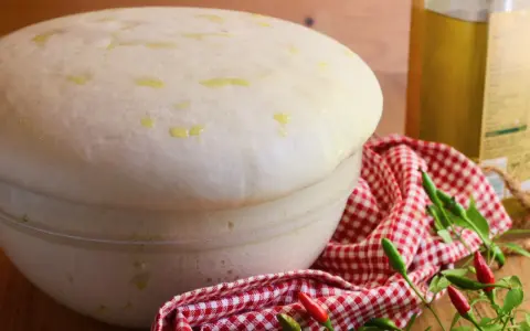 Impasto lievitato per pizza con lievito di birra, soffice e profumato, pronto per essere infornato. Olio e peperoncini completano la scena.