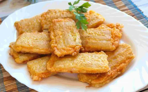 Pencas rellenas doradas y crujientes, apiladas en un plato blanco, con una ramita de perejil fresco.