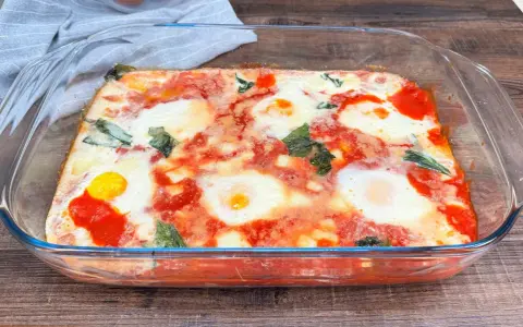 Uova alla contadina appena sfornate in teglia di vetro, con pomodoro e basilico.