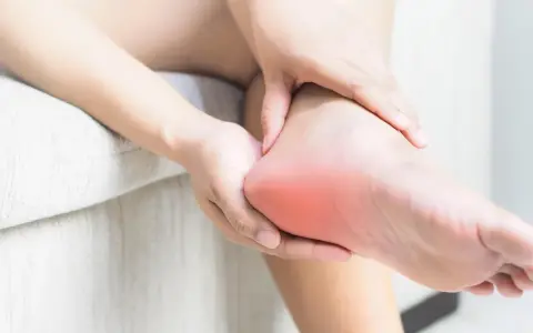 Dłoń masuje bolesną piętę, gdzie może występować neuropatia Baxtera.