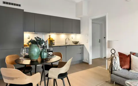 Arredare una sala moderna con cucina a vista: tavolo rotondo con sedie in legno, vasi verdi e candele.