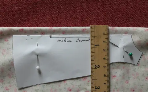 Patron de couture marqué "milieu devant", épinglé sur un tissu fleuri. Une règle en bois mesure la pièce.