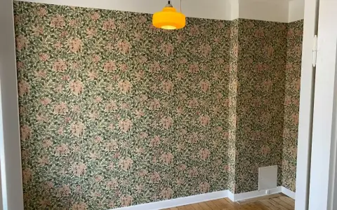 Ett rum med blommig tapet och en gul lampa. Undrar vad kostar det att måla om ett rum?