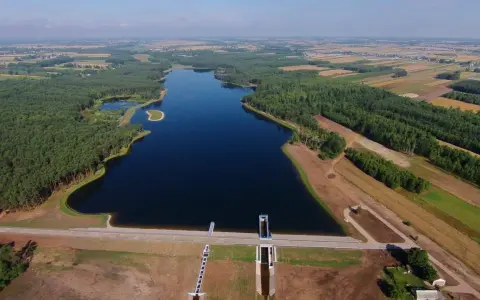 Widok z lotu ptaka na zalew Jagodno otoczony lasem i polami. Na pierwszym planie zapora z budowlami technicznymi.