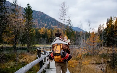 Ojciec z dzieckiem na plecach spaceruje drewnianą kładką pośród jesiennych lasów. Tatry z dzieckiem to piękna przygoda.