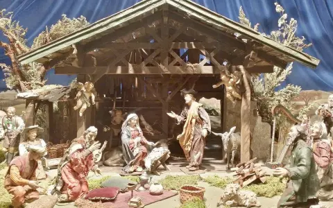Krippenszene mit Maria, Josef und dem Jesuskind. Engel schweben über der Szene, die an Weihnachten im Mittelalter erinnert. Hirten und Musiker sind versammelt.