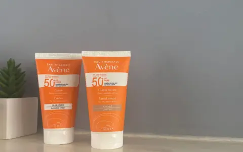Deux tubes de spray solaire invisible SPF 50 Avène, l'un teinté, l'autre non, pour une protection optimale.