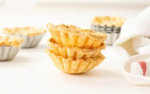 Montón de tartaletas de hojaldre listas para rellenar con crema pastelera.