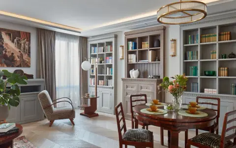 Elegancki salon w stylu art deco z dwoma regałami pełnymi książek, okrągłym stołem i wygodnym fotelem.