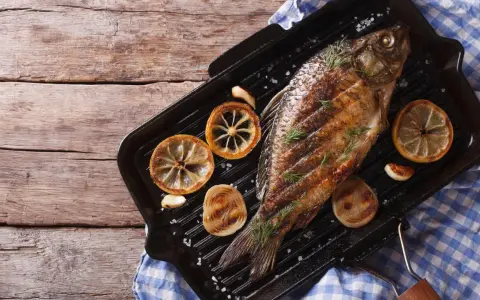 Gegrillter Karpfen mit Zitronenscheiben und Kräutern auf einer Grillpfanne. Ein Genuss, Karpfen zu essen!