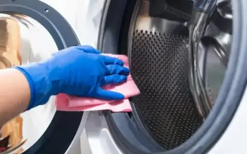 Mano con guante azul limpiando la goma de la lavadora con un paño rosa.
