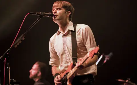 Ben Gibbard chante et joue de la guitare sur scène, éclairé par les projecteurs.