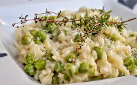 Kremowe risotto z groszkiem, posypane parmezanem i udekorowane gałązką tymianku. Pyszne danie, które zachwyca smakiem.