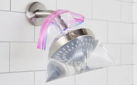 A shower head is submerged in a plastic bag filled with vinegar, secured with a rubber band. This shows how to clean shower head vinegar for a sparkling finish.