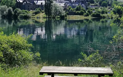 Un banco de madera invita a contemplar el embalse de Lanuza, con un pueblo de tejados grises reflejado en sus tranquilas aguas verdes.