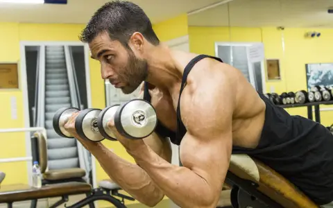 Man utför spider curls med hantlar på ett gym.