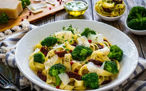 Pyszny makaron z brokułami, suszonymi pomidorami i parmezanem, udekorowany świeżymi ziołami.