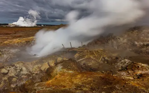 Gunnuhver hot springs: para buchująca z ziemi, zniszczona drewniana konstrukcja, chmury burzowe nad krajobrazem.