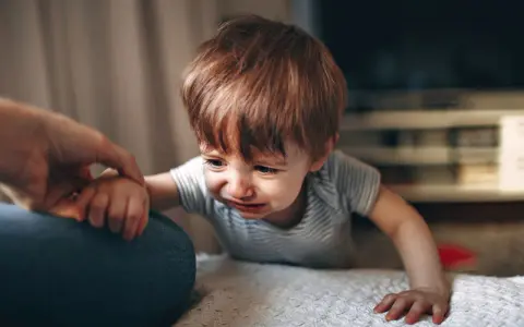 Małe dziecko płacze, a dorosły chwyta je za rękę. Widoczny jest szarpanie dziecka w nerwach.