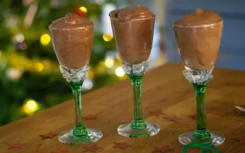 Tre glas med krämig chokladmousse, perfekta för ett enkelt chokladmousse recept. Julbelysning i bakgrunden skapar en festlig stämning.