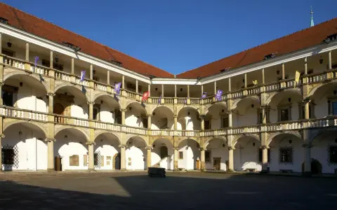 Dziedziniec renesansowego zamku z arkadowymi krużgankami, ozdobiony flagami.