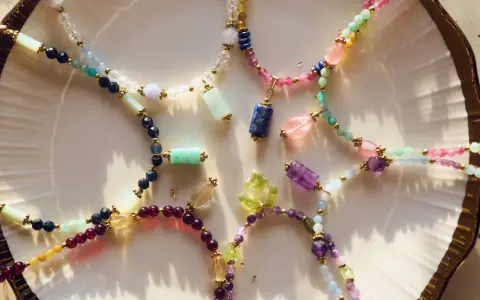 Kolorowe naszyjniki z kamieni szlachetnych, w tym lapis lazuli znak zodiaku, ułożone na talerzu.