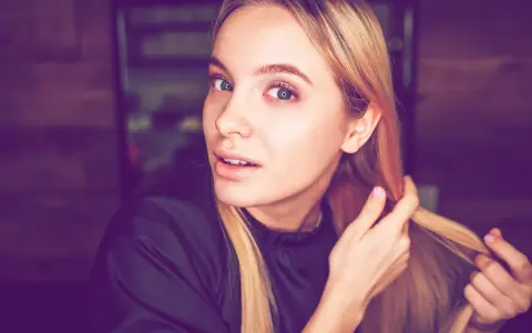 Junge Frau mit blonden Haaren, die sich die Haare für die Olaplex No. 0 Anwendung zurechtmacht.