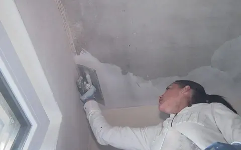 Frau spachtelt mit einem Werkzeug die Betondecke, um sie für die weitere Bearbeitung vorzubereiten.