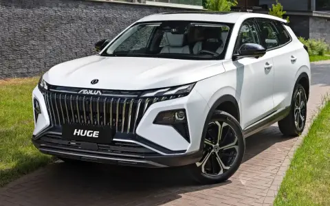 Nowy, biały chinski suv z imponującym grillem i felgami stoi na podjeździe.