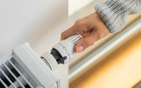 Dłoń reguluje termostat grzejnika, przygotowując się do wymiany termostatu.