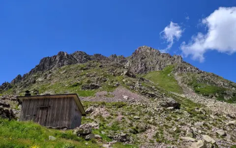 Bivacco Paolo e Nicola, un rifugio in legno ai piedi di montagne rocciose sotto un cielo azzurro.
