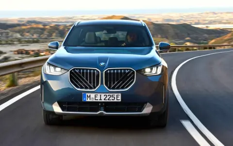 Nowy **BMW X3 2025** w kolorze granatowym jedzie krętą drogą pośród pustynnych krajobrazów.