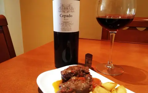 Un plato de carrilleras estofadas con patatas, acompañado de una copa de vino tinto Cepado Mencía, ideal para maridar.
