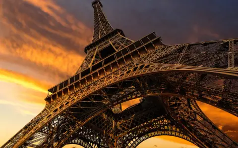 La Torre Eiffel, una icónica estructura de hierro forjado, se alza majestuosa contra un cielo anaranjado al atardecer.
