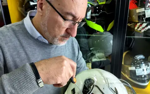 Uomo con cacciavite regola la visiera di un casco bianco, assicurandosi che il casco debba avere la visiera priva di graffi.