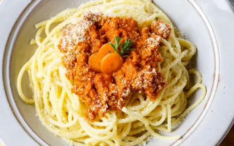 Spaghetti Bolognese, zubereitet im Thermomix, mit Karottenscheiben und Petersilie garniert.