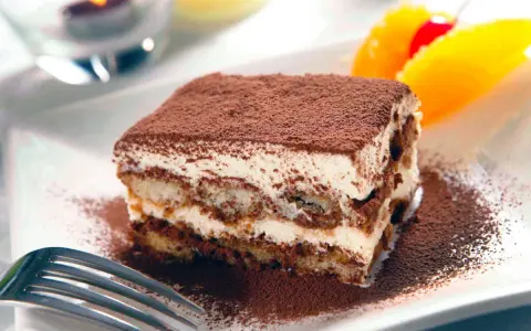 En bit krämig tiramisu, pudrad med kakao, serveras med frukt. Perfekt dryck till tiramisu.