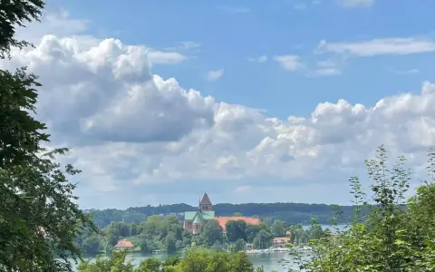 Blick auf die Ratzeburg Altstadt mit Domkirche, umgeben von grünen Bäumen und dem See unter einem dramatischen Wolkenhimmel.