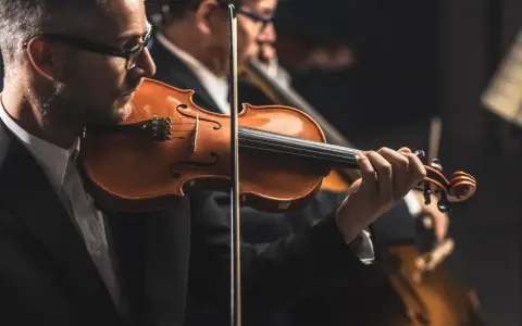 Skrzypek grający melodię, która mogłaby być jedną z piosenek o Krakowie. W tle inni muzycy orkiestry.