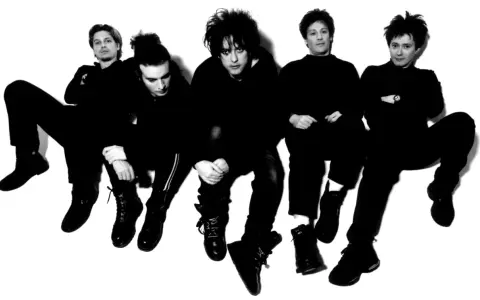 Les membres de The Cure, cinq silhouettes sombres aux coiffures distinctives, posent en groupe, l'air pensif.